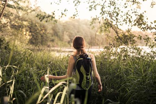 Ragazza con zaino in spalla cammina nella foresta vicino ad un fiume praticando il Forest Bathing