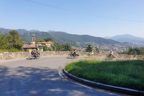 Un gruppo di persone in bicicletta pedalano lungo una strada in salita in un antico borgo bergamasco