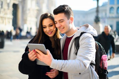 Una giovane coppia in Piazza Duomo a Milano, stanno partecipando ad un escape game urbano e guardano un tablet per risolvere enigmi e rompicapi