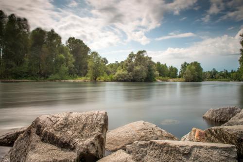 Fotografia del Parco del Ticino massi in primo piano a fuoco, fiume e riva opposta sfocata