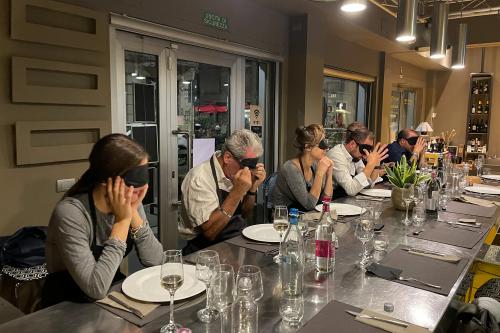 Un gruppo di persone sono sedute ad un tavolo di una scuola di cucina con una benda nera sugli occhi