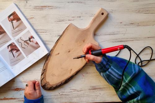 Una ragazza con il pirografo in mano sta per iniziare ad incidere un tagliere di legno durante il corso di pirografia in Val Seriana vicino Bergamo