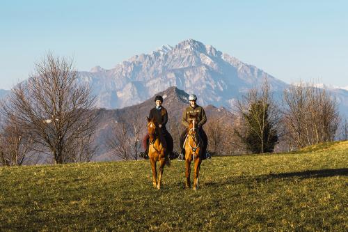 Due ragazzi in sella a dei cavalli arabi purosangue passeggiano nella natura sullo sfondo le montagne del Lago di Como