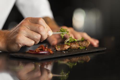 Mani di uno chef professionista che dopo aver spiegato come cuocere la carne durante il corso di cucina a Milano spiega come impiattare