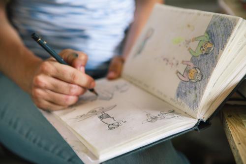 Una ragazza seduta che tiene in mano una matita e sta disegnando una illustrazione su un libro di bozze durante un corso di illustrazione vicino a Como