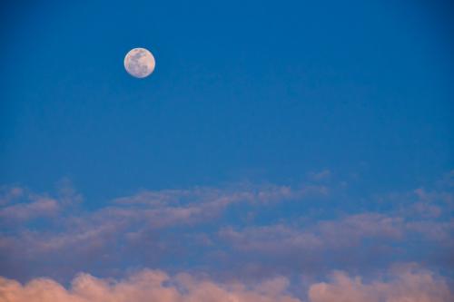 La luna nel cielo azzurro blu della Lombardia in basso le nuvole rosa illuminate dalla luce del sole al tramonto