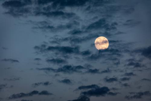 Luna piena che si nasconde dietro le nuvole scure nel cielo azzurro blu di primavera vicino Brescia in Lombardia