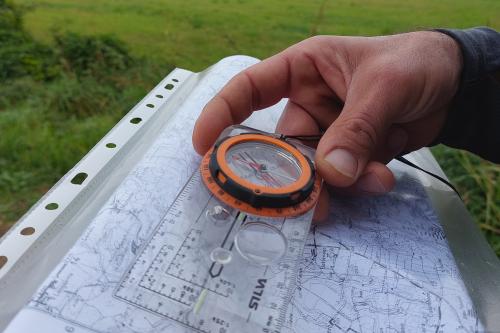 Un uomo tiene in mano una Bussola e una mappa durante una esperienza di orienteering in Lombardia