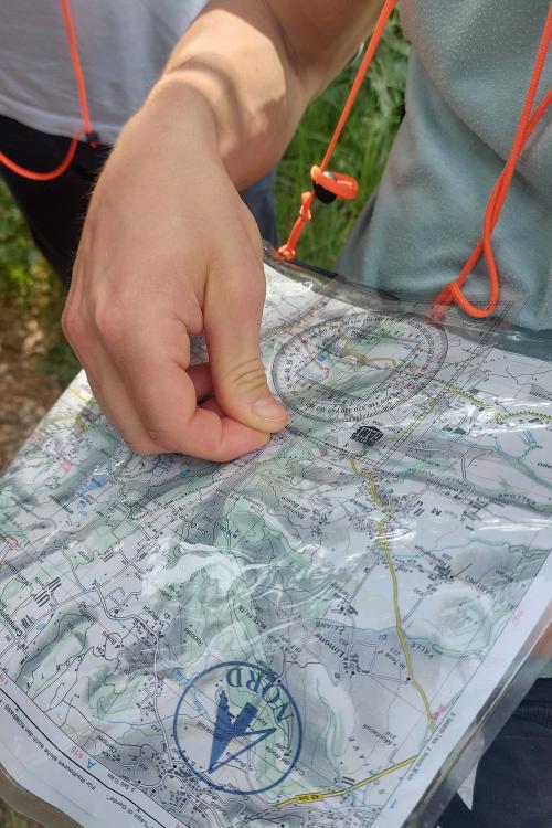 Un ragazzo munito di mappa bussola e coordinatometro sta partecipando ad una esperienza di orienteering in Lombardia