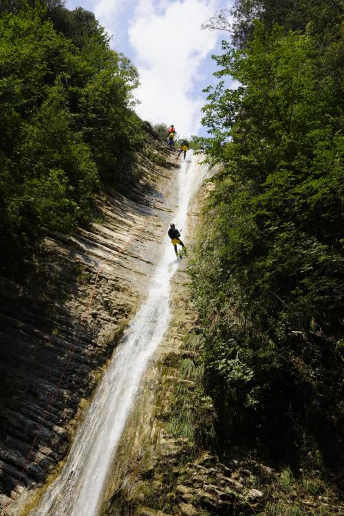 Un ragazzo ancorato ad una corda durante una esperienza di canyoning vicino al Lago di Garda si cala lungo una cascata