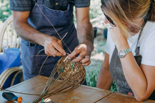 Un artigiano durante un corso di intreccio sul Lago di Como mostra ad una donna come creare un cesto in salice naturale