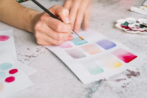 Mano di una ragazza che tiene un pennello e dipinge sulla carta con un acquerello durante il corso creativo in Lombardia non lontano da Como
