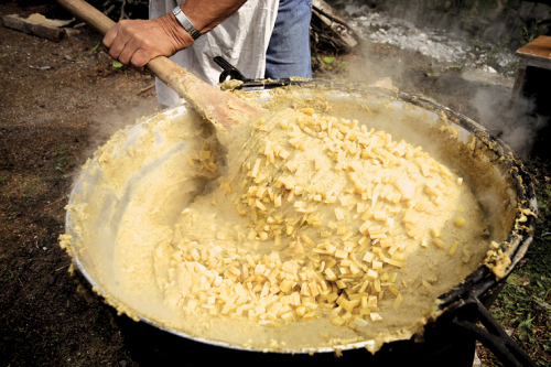 Una persona sta mescolando la polenta taragna con il formaggio Storico Ribelle cotta sul fuoco dentro un grande paiolo
