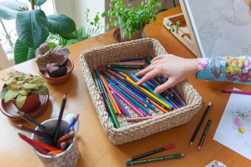 Mani di una ragazza che tocca delle matite colorate in attesa di trovare l'ispirazione per la sua nuova illustrazione botanica