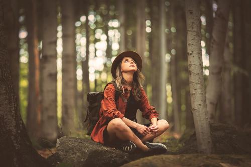 Una ragazza con lo zaino in spalla è seduta su un masso nel Parco del Ticino in Lombardia vicino a Milano mentre sta entrando in contatto con la natura attraverso la pratica del Forest Bathing