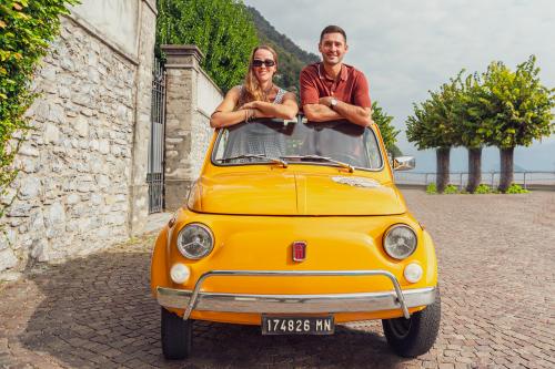 Due ragazzi a bordo di una Fiat 50 d'epoca gialla noleggiata a Como in Lombardia si rilassano osservando il bellissimo panorama del lago