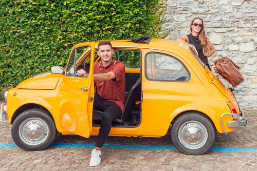 Una coppia di ragazzi a bordo di una Fiat 500 d'epoca noleggiata a Como in Lombardia per un giro panoramico sul lago