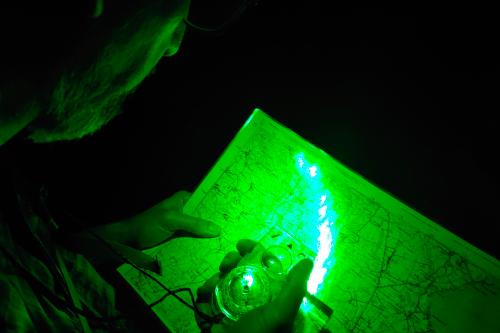 Un uomo durante il corso di orienteering notturno vicino al Lago di Garda in Lombardia sta imparando ad orientarsi con mappa e bussola nel buio solo illuminato da una torcia frontale