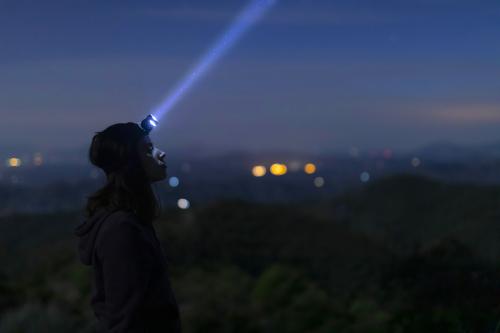 Una ragazza che indossa una torcia frontale osserva il cielo notturno durante il corso di orienteering vicino al Lago di Garda in Lombardia